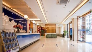 Un espace d’accueil d’hôtel comprenant un comptoir de réception, un comptoir bleu, un canapé vert et une vitrine en verre.