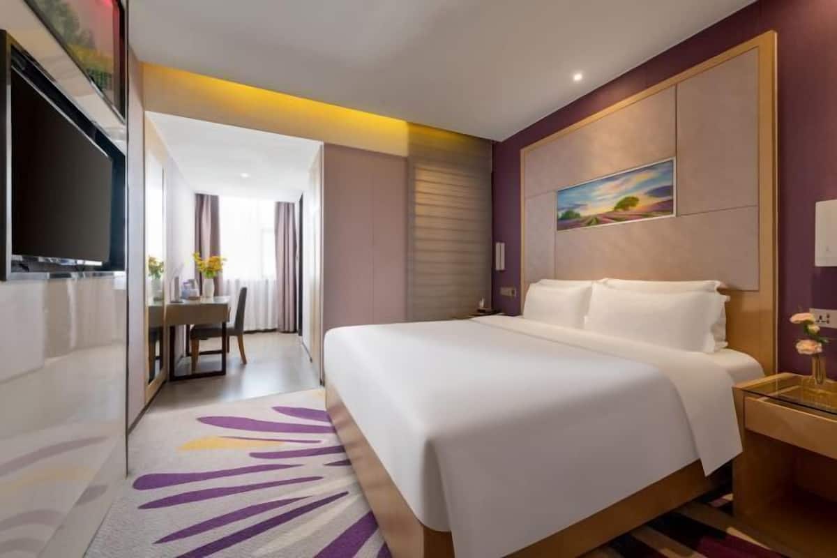 A hotel room with a large bed, a desk with a chair, and a television on the wall.
