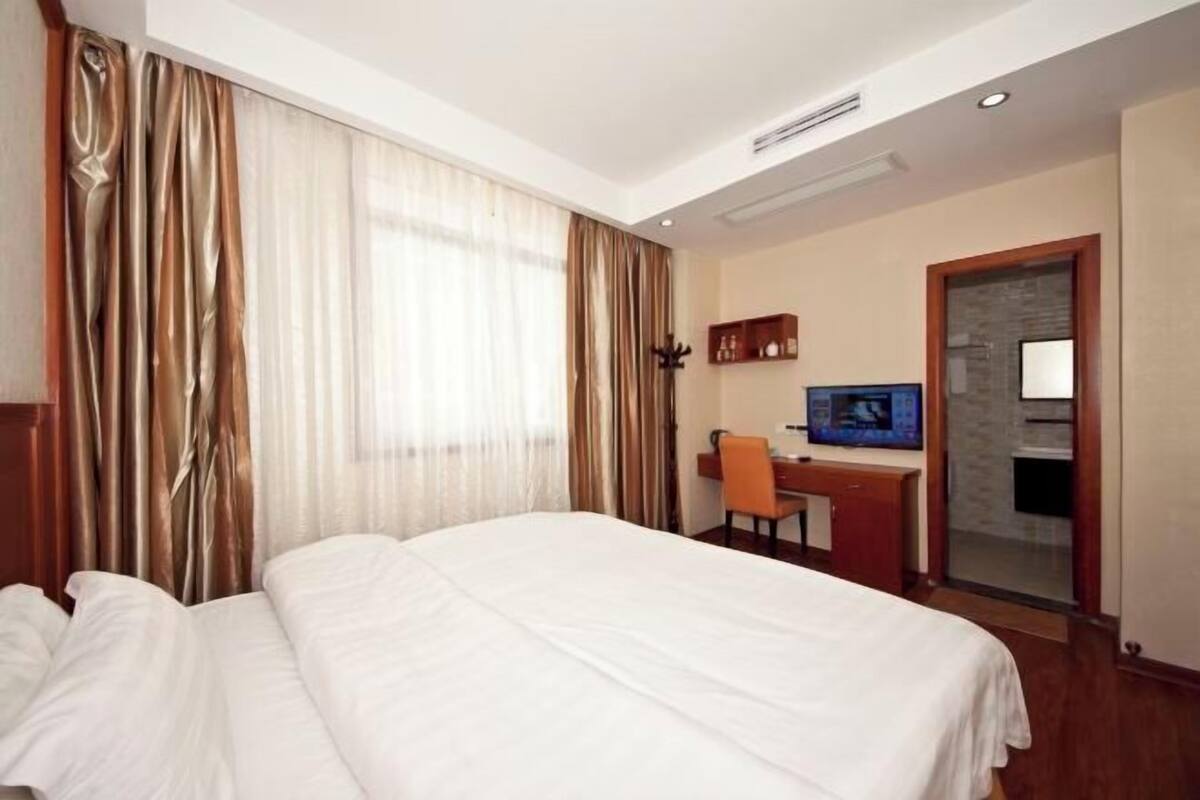A hotel room with a bed, a desk, a chair, and a television.