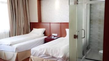 Quarto de hotel com duas camas de solteiro, cabeceira de madeira, box de vidro para o chuveiro e parede com padrão.