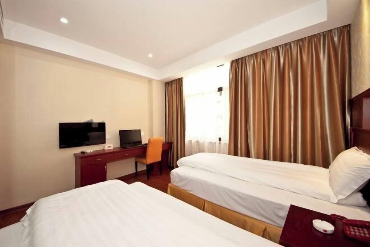 A hotel room with two beds, a desk with a chair, a television, and a window with curtains.