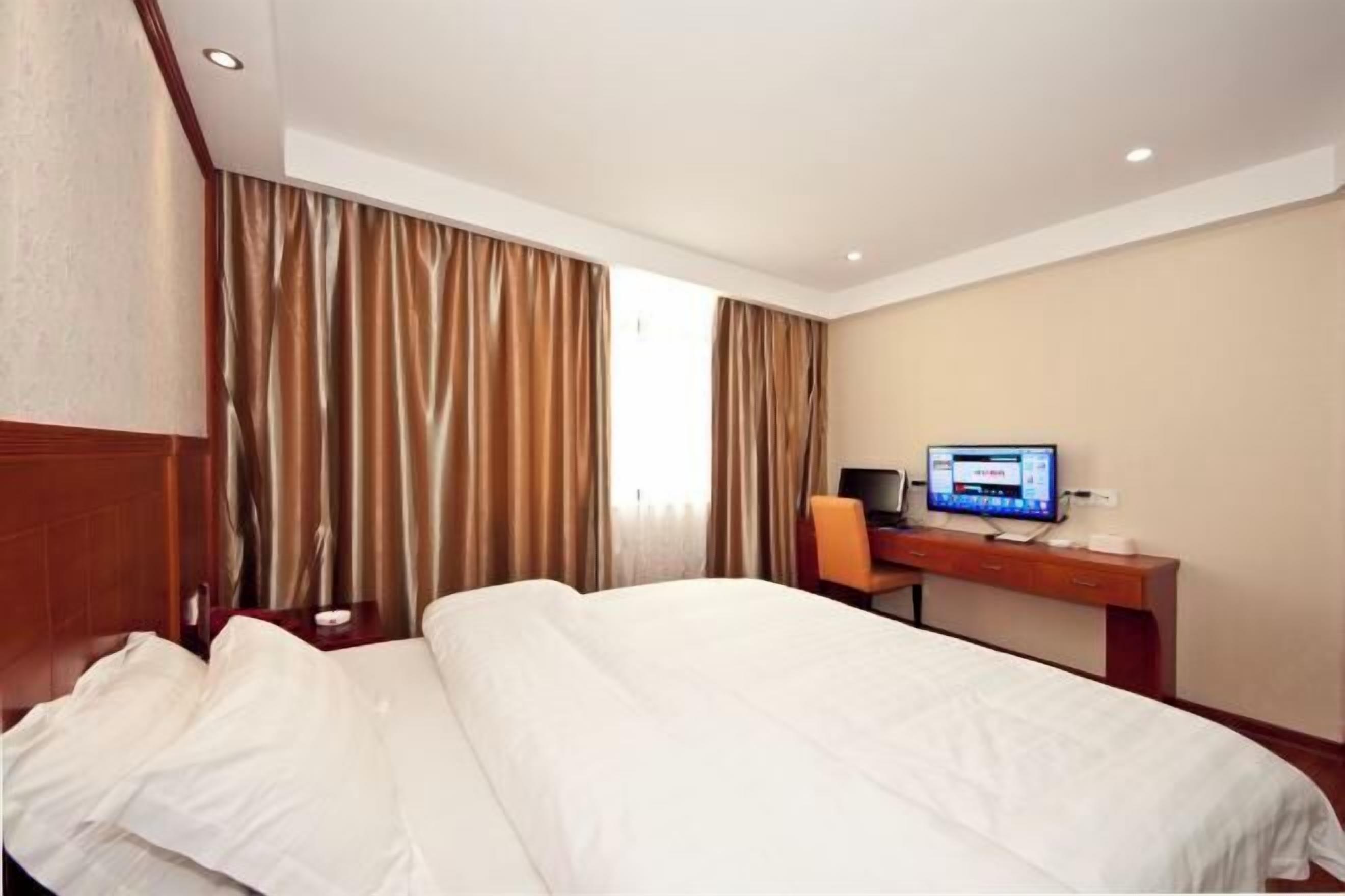 A hotel room with a bed, a desk with a computer, and curtains.
