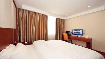 A hotel room with a bed, a desk with a computer, and curtains.