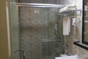Een douche met glazen wanden en deur, een handdoekrek met handdoeken, en een toilet met een handdoek erop.