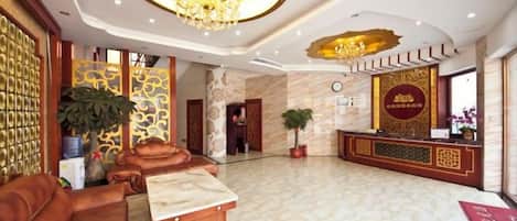 A hotel lobby with a reception desk, seating area, and a chandelier.