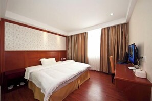 Ein Hotelzimmer mit Doppelbett, Holz-Kopfteil, Schreibtisch mit Computer und Fernseher.