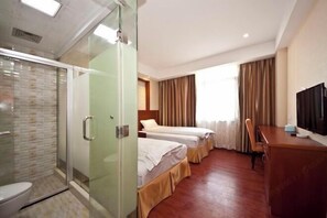Ein Hotelzimmer mit Dusche, zwei Betten, einem Schreibtisch und einem Fernseher.