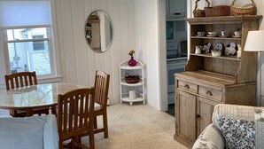 Een eetgedeelte met een ronde tafel en stoelen, een houten kast met planken en een gestreept bankje.