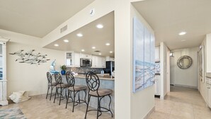 Een ruime keuken met een centraal eiland, witte kasten en een decoratief kunstwerk.