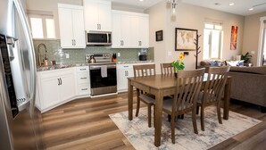 A modern kitchen with white cabinets, stainless steel appliances, and a wooden dining table.