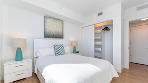 Une chambre moderne avec un grand lit, des tables de chevet blanches, un placard avec espace pour suspendre les vêtements et une œuvre d’art au plafond.