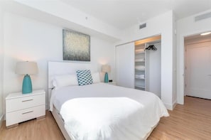 Ein modernes Schlafzimmer mit einem großen Bett, weißen Nachttischen, einem Kleiderschrank mit Platz zum Aufhängen und einem Kunstwerk an der Decke.