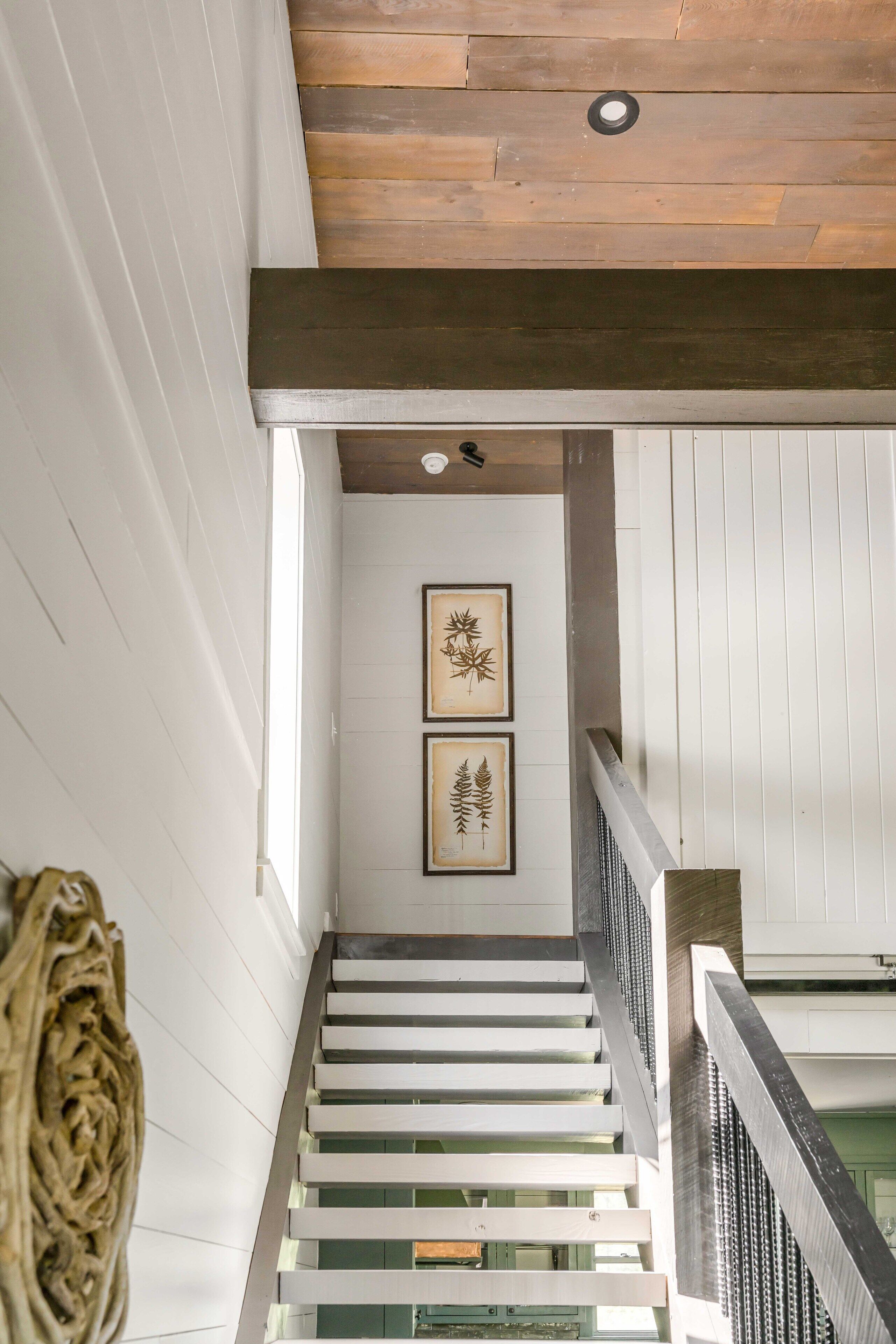 Eine Treppe mit weißen Geländern und Holzbalken, die zu einem Raum führt, der mit gerahmten Pflanzenbildern an der Wand dekoriert ist.
