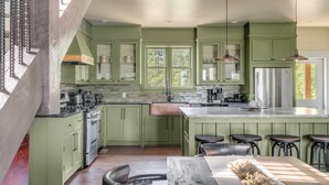 A modern kitchen with green cabinets, a stainless steel refrigerator, and a bar area with stools.