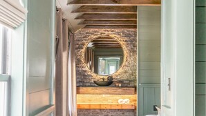 A hallway with wooden flooring, a stone wall, and a circular mirror.