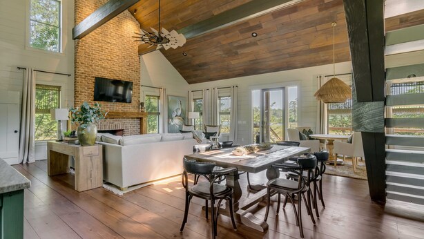 A spacious kitchen with a large island, wooden ceiling beams, and a brick wall.