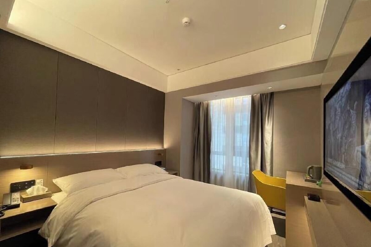 Une chambre d’hôtel moderne dotée d’un grand lit, d’un bureau avec une chaise, d’une télévision et d’une fenêtre avec des rideaux.