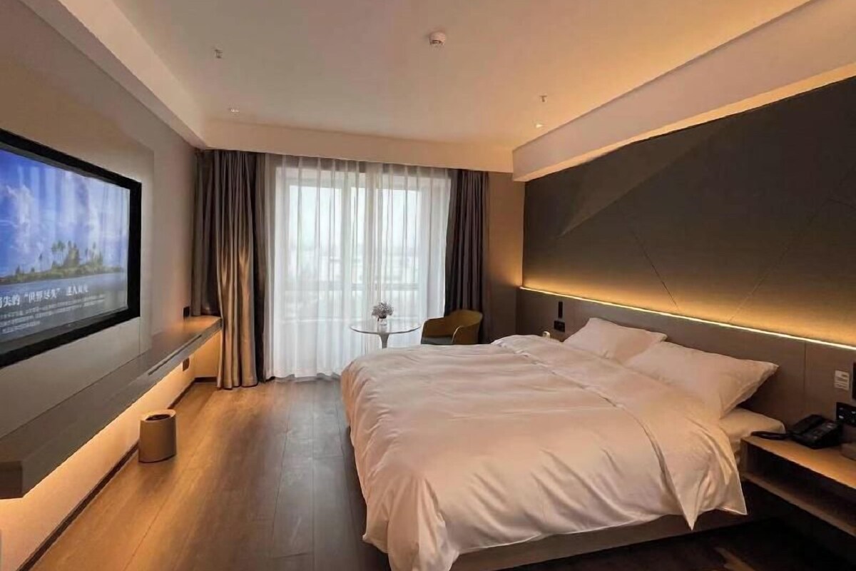 Une chambre d’hôtel moderne avec un grand lit, un téléviseur à écran plat fixé au mur, une petite table ronde et une chaise.