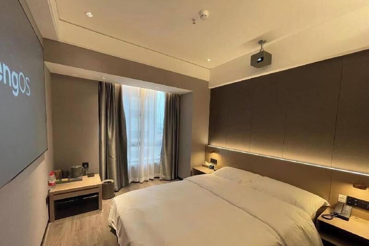 A modern hotel room with a large bed, a desk, a chair, a TV, and a window with curtains.