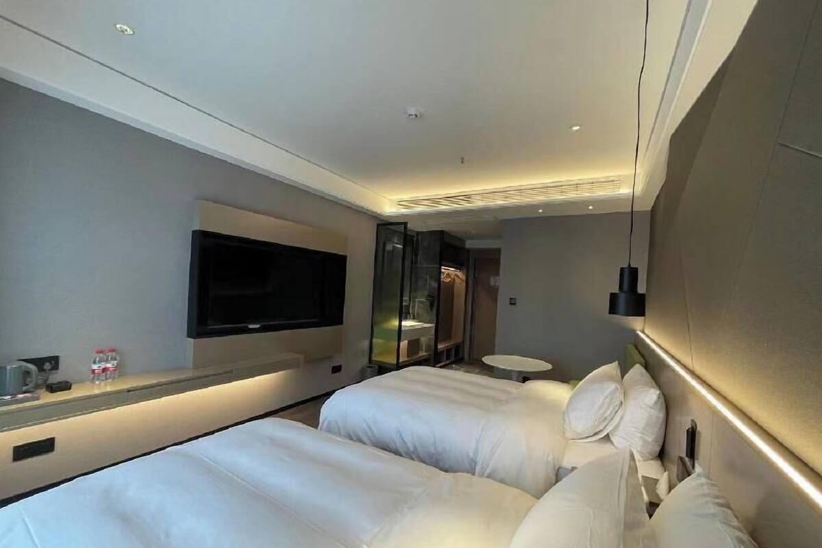 A hotel room with two beds, a TV mounted on the wall, a glass partition, and a small round table.