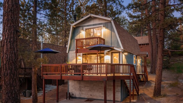 Une cabane à deux étages dotée d’un balcon, d’une terrasse en bois et d’un petit porche.