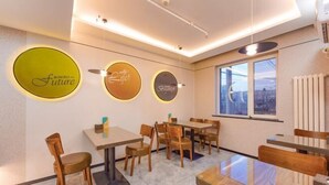 A restaurant interior with round tables and chairs, a city view through large windows, and illuminated wall signs.