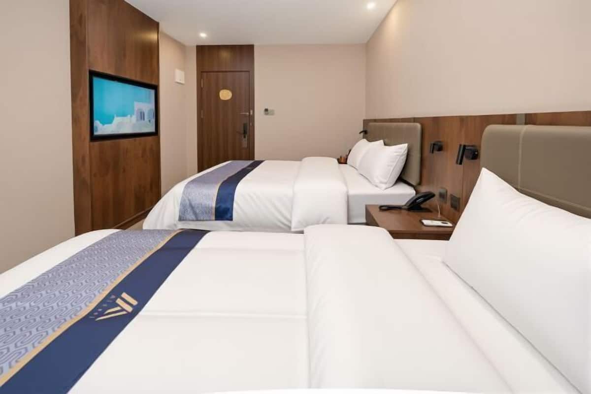 A hotel room with two beds, a wooden headboard, a wall-mounted TV, and a bedside table with a phone.