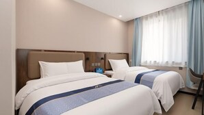 A hotel room with two beds, a nightstand, a chair, and a window with curtains.
