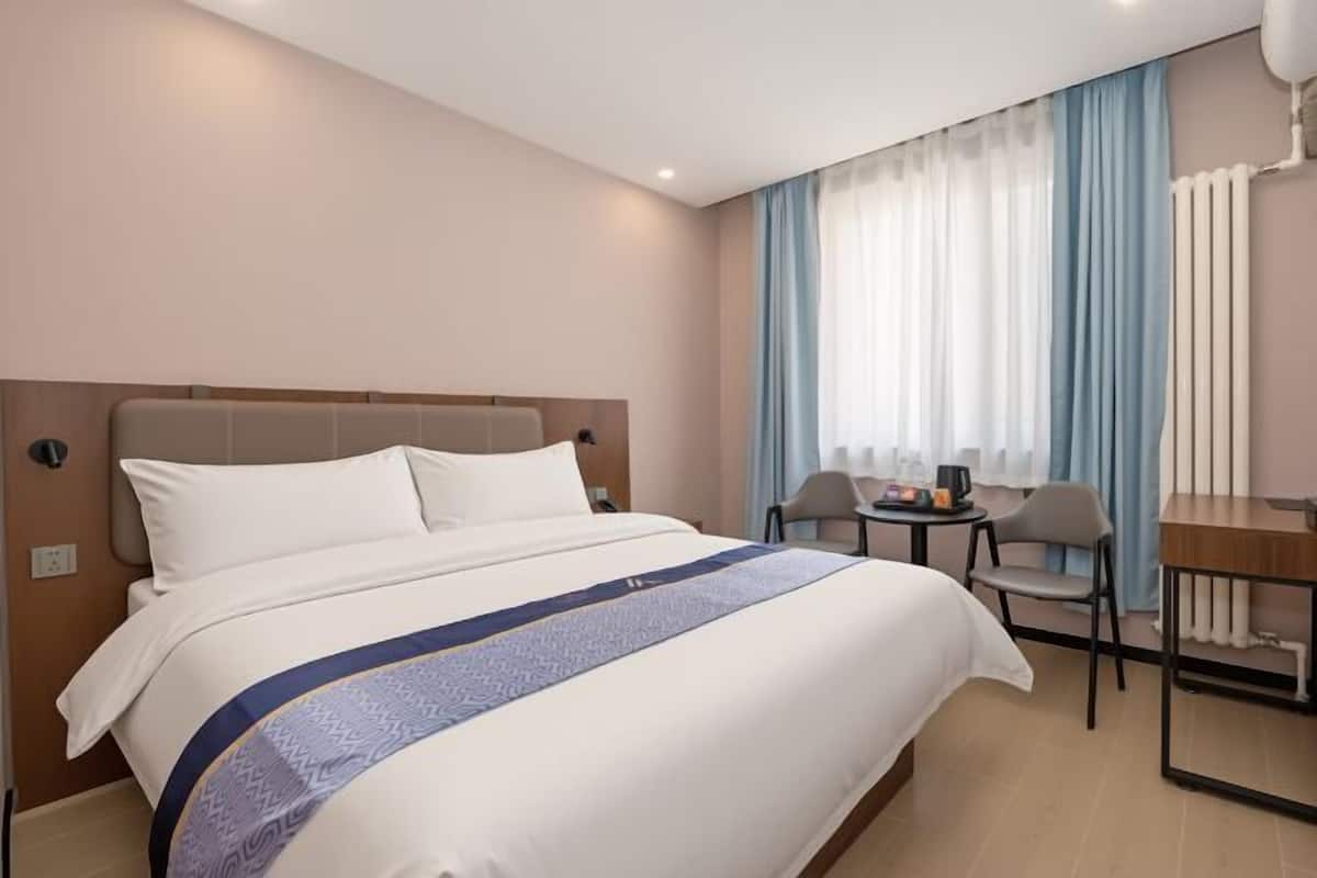 A hotel room with a bed, a desk, chairs, and a window with curtains.