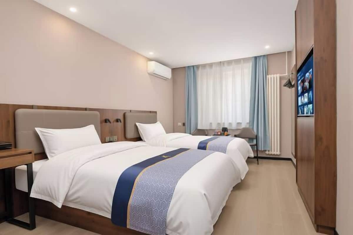 A hotel room with two beds, a desk, a TV, and a wardrobe.