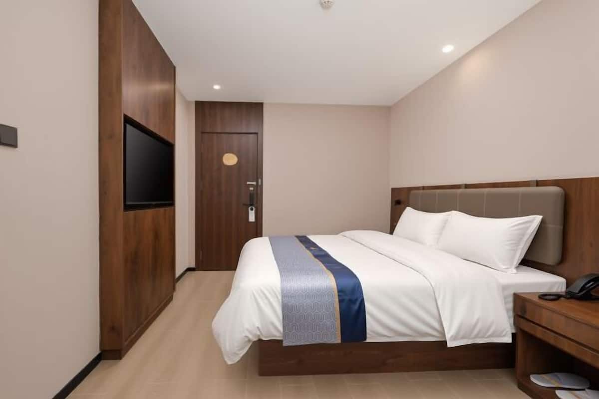 A hotel room with a bed, a bedside table, a TV mounted on the wall, and a door.