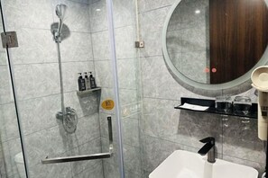 A bathroom with a glass-enclosed shower, a round mirror, a white sink, and a shelf with toiletries. - Aifeel Hotel (Beijing Lishuiqiao Subway Station) (Beijing)