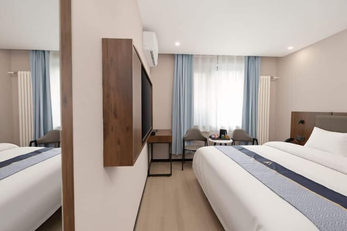 A hotel room with two beds, a desk, a chair, a TV, and a window with curtains.