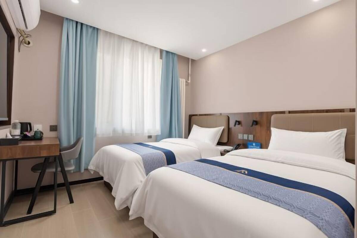 A hotel room with two beds, a desk, a chair, a coffee maker, and a window with curtains.