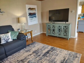 Un salon avec un canapé foncé, un tapis à motifs, un meuble turquoise et un grand téléviseur fixé au mur.