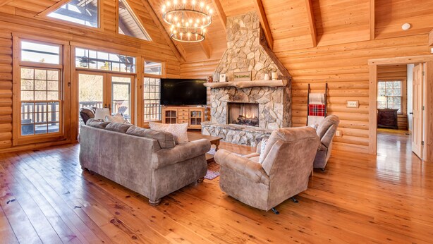 A spacious log cabin interior with a stone fireplace, wooden floors, and a large TV. - Wooded Cabin: Mtn Views, Hot Tub & 2 Decks! (Sapphire)