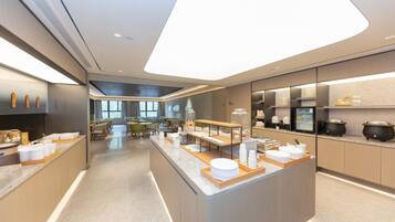 A modern hotel kitchen with a central island, dining area, and kitchen appliances.