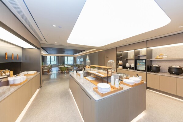 A modern hotel kitchen with a central island, dining area, and kitchen appliances. - Ji Hotel (Kaifeng)