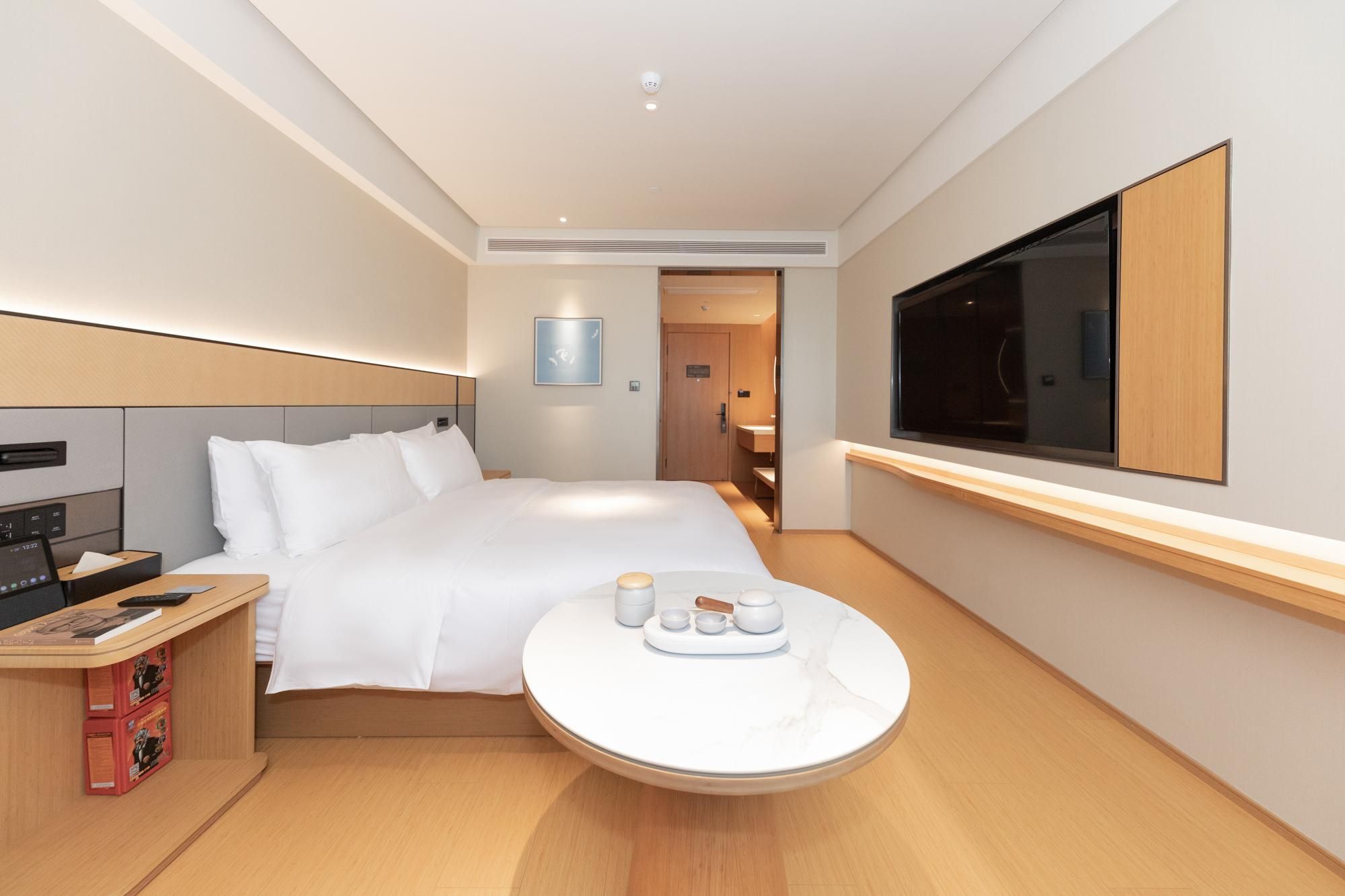 A modern hotel room with a bed, bedside table, and a round table with tea set.