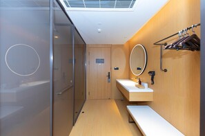 A modern bathroom with a glass shower enclosure, a wooden vanity with a mirror, and a bench. - Ji Hotel (Kaifeng)