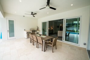 A spacious patio with a dining table and chairs, a ceiling fan, and a sliding glass door leading to a pool area.