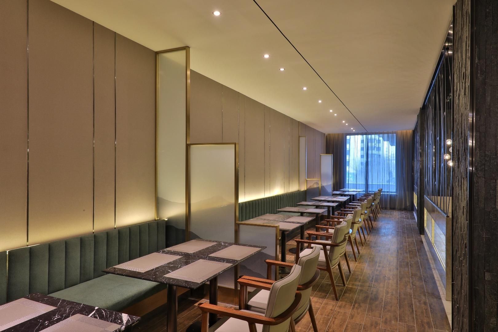 Habitación de hotel moderna con una larga mesa de comedor, asientos acolchados y un amplio ventanal con vistas.