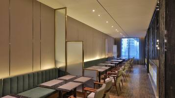 Habitación de hotel moderna con una larga mesa de comedor, asientos acolchados y un amplio ventanal con vistas.