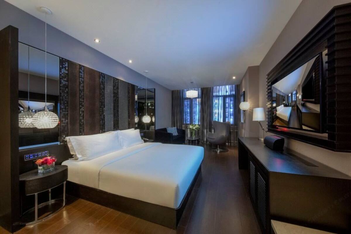 A modern hotel room with a large bed, a TV, a desk, and a seating area.