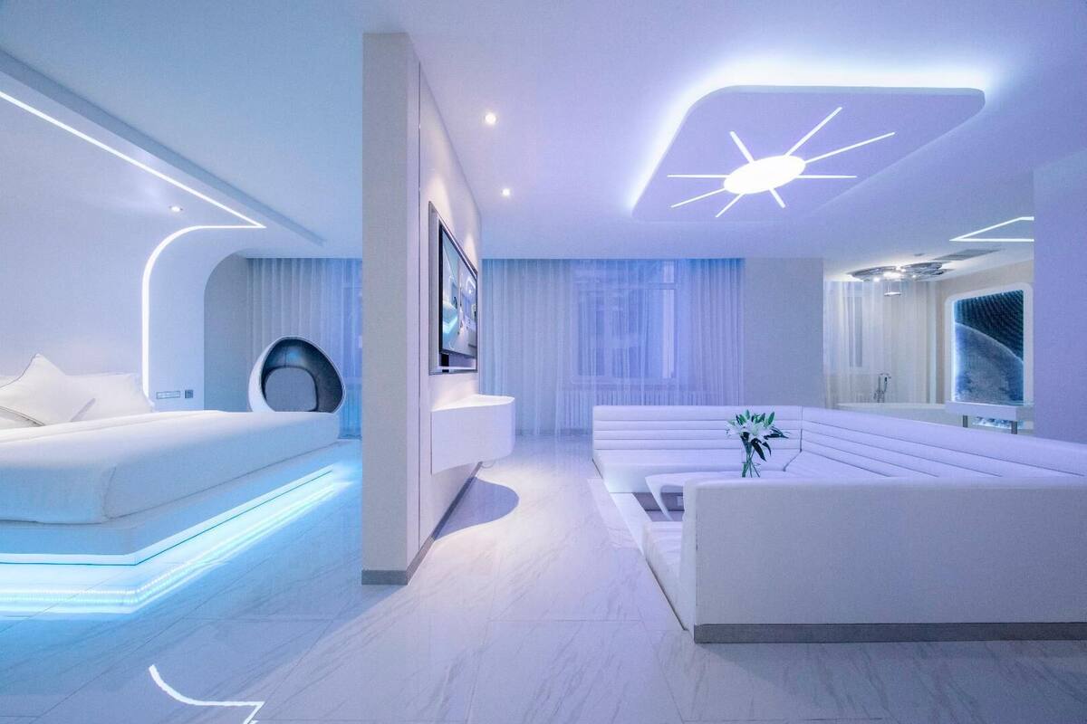 A modern, minimalist bedroom with a bed, a seating area, and a large window.
