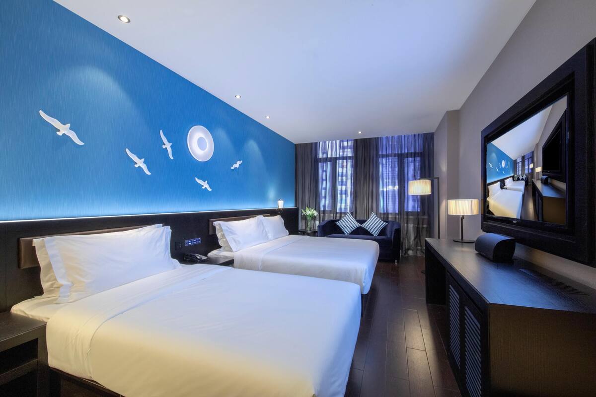 A hotel room with two beds, a TV, and a wall with a blue mural.