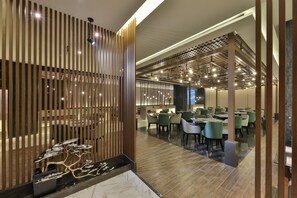 A modern interior with a wooden partition, a dining area with tables and chairs, and a ceiling with exposed beams and lighting.