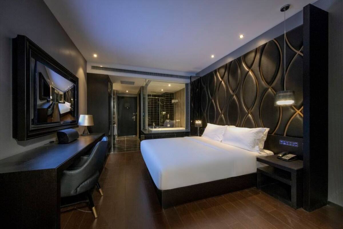 A modern hotel room with a large bed, a desk with a chair, a mirror, and a wall with a unique pattern.
