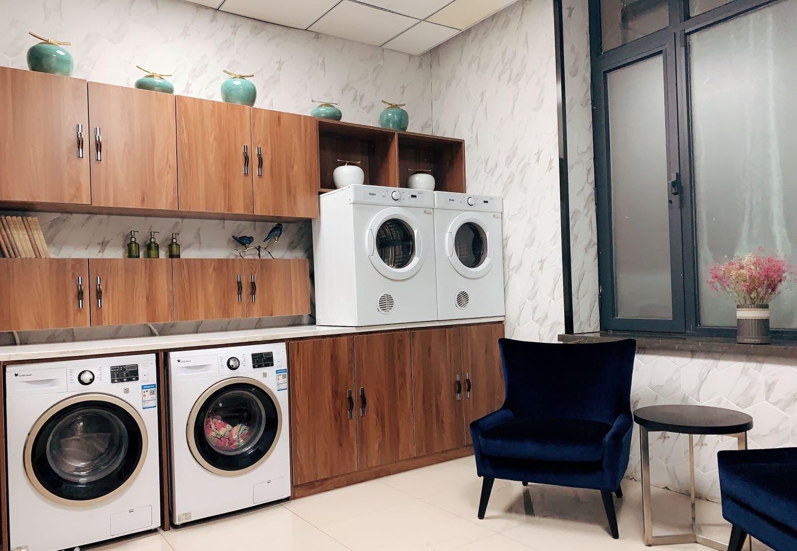 Une buanderie équipée de deux machines à laver à chargement frontal, de meubles en bois et d’une chaise bleue.