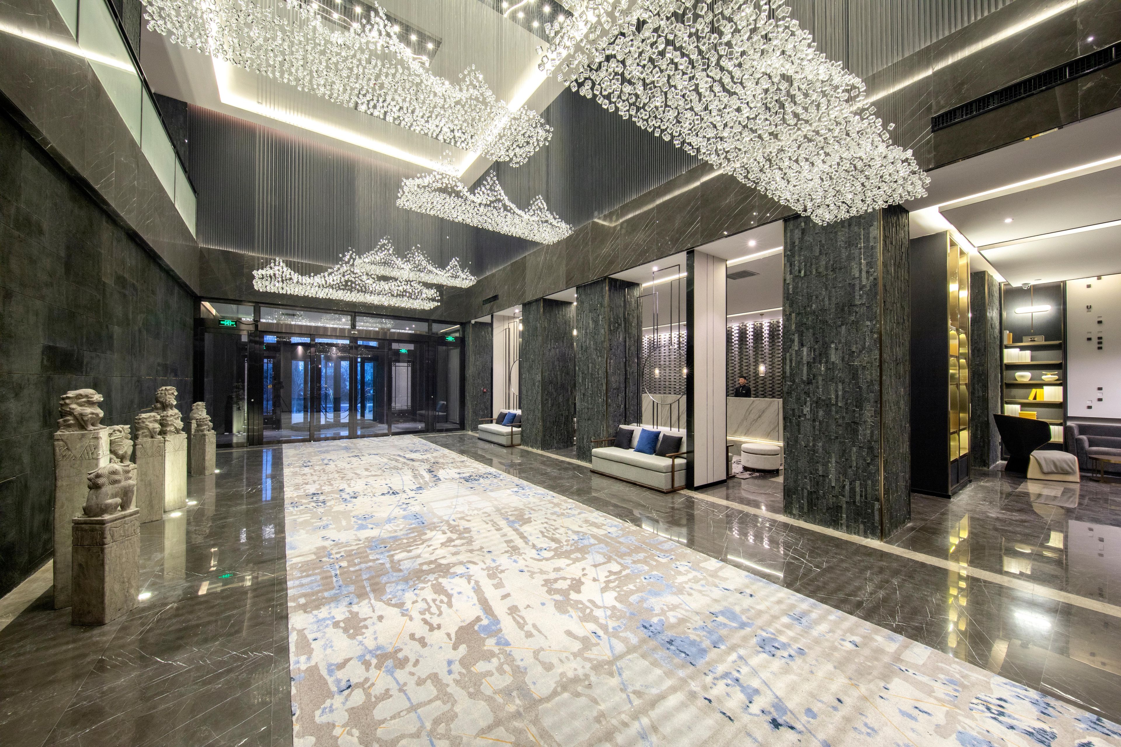 Un vestíbulo amplio con suelo reflectante, una zona de estar central y un moderno candelabro.